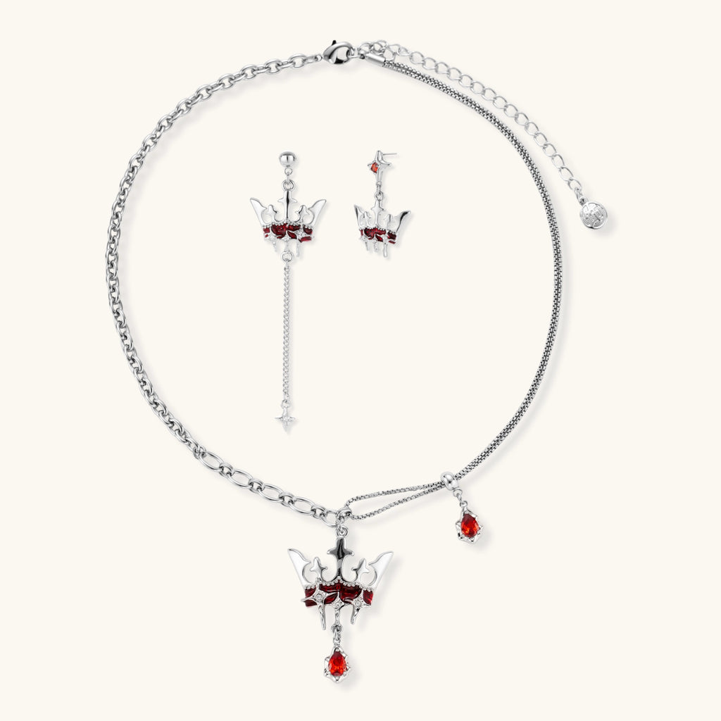 Silver-tone crown pendant with red zirconia stones and matching asymmetrical earrings on cream background
