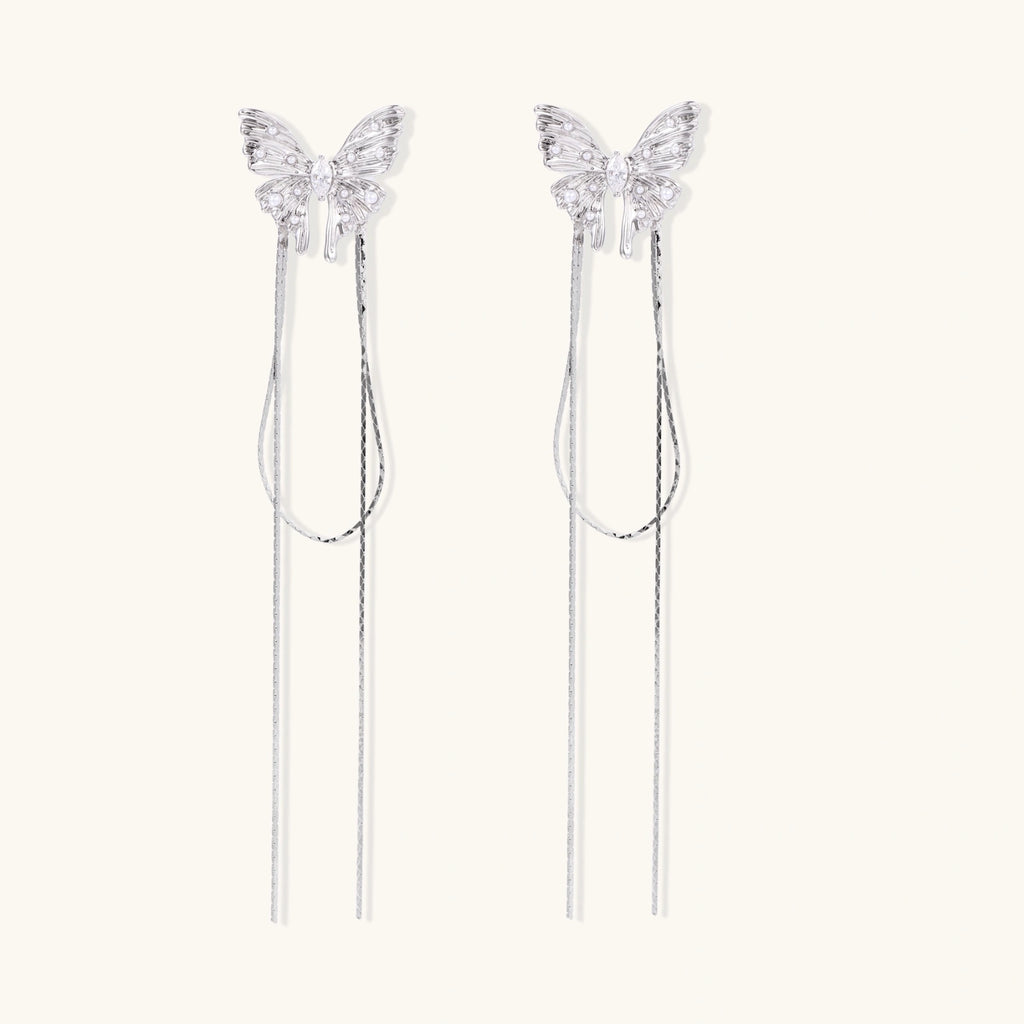 Pair of silver threader earrings with crystal butterfly tops and long chain drops on cream background.