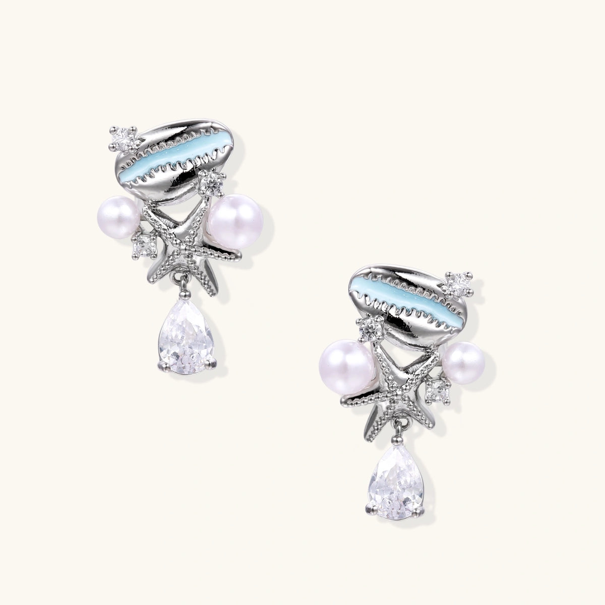 Ocean-themed drop earrings with blue enamel shells, white pearls, starfish charms and crystal teardrops on white background.