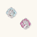 Silver unicorn stud earrings with pastel blue and pink enamel stones in sunburst prong settings on cream background